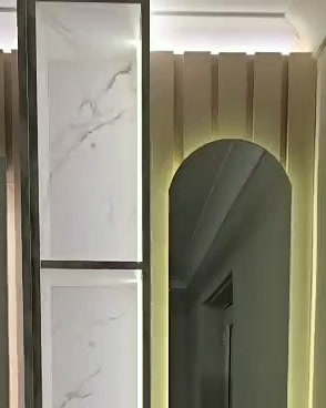 Lit glass display column beside an arched mirror panel, under a warm LED cove on fluted panelling