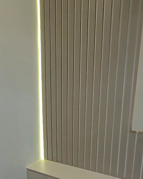 Full-height oak-tone slats washed by a hidden vertical LED strip
